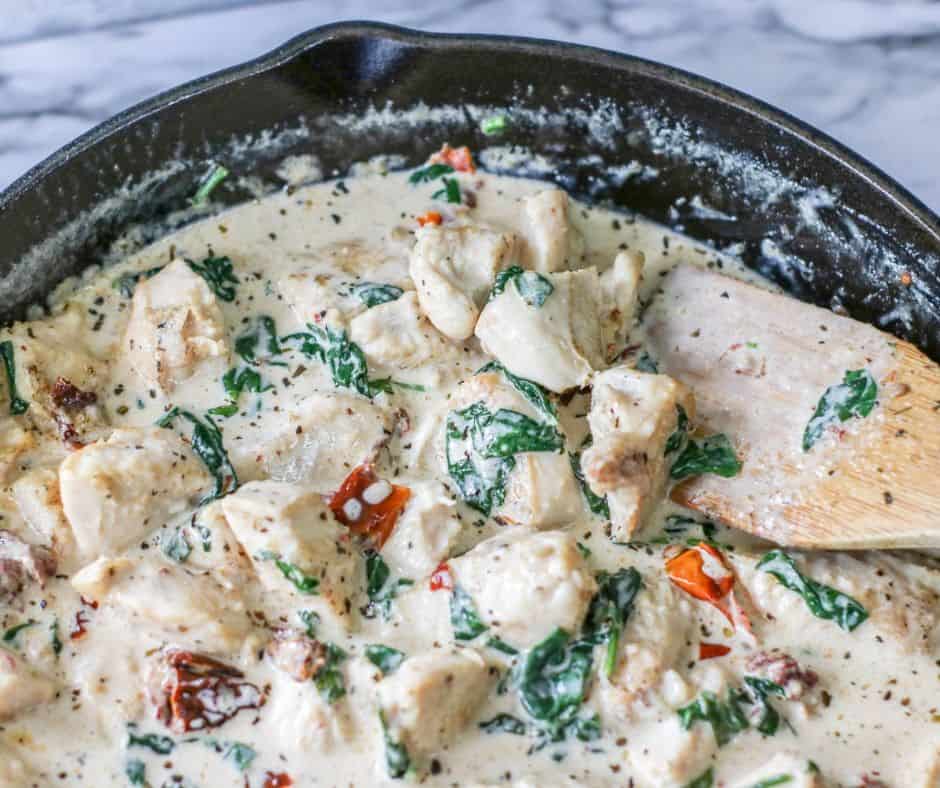 skillet with Tuscan chicken in creamy garlic sauce in it, with fresh spinach and bacon for color