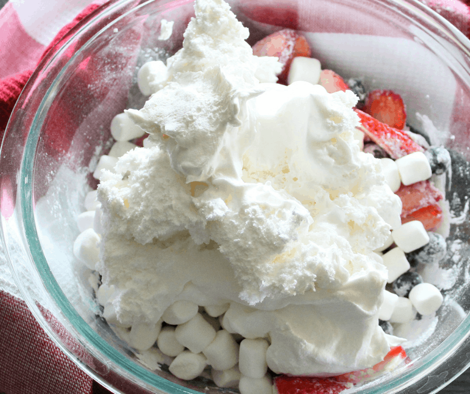 adding the whipped cream to the bowl full of berries and pudding mix 