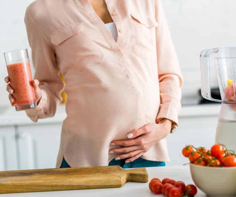 woman drinking a fruit smoothie while massaging her pregnant belly because she is having a healthy pregnancy