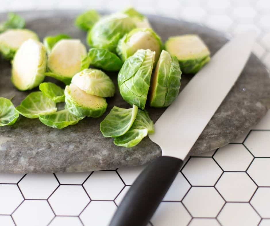 knife and cutting board with halved brussel sprouts being prepped for roasting