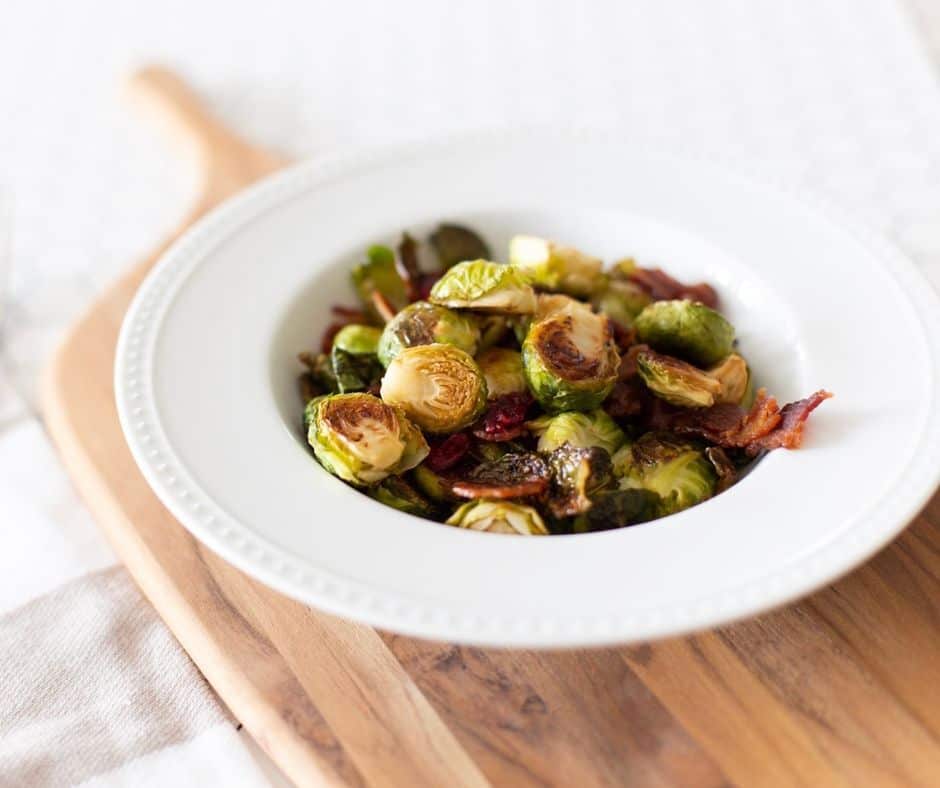 brussel sprouts with bacon in a white bowl on a wooden cutting board