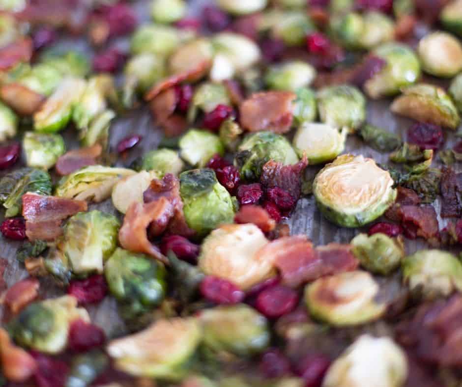 roasted brussel sprouts on a baking sheet with bacon crumbles and cranberries in a balsamic glaze that has caramelized