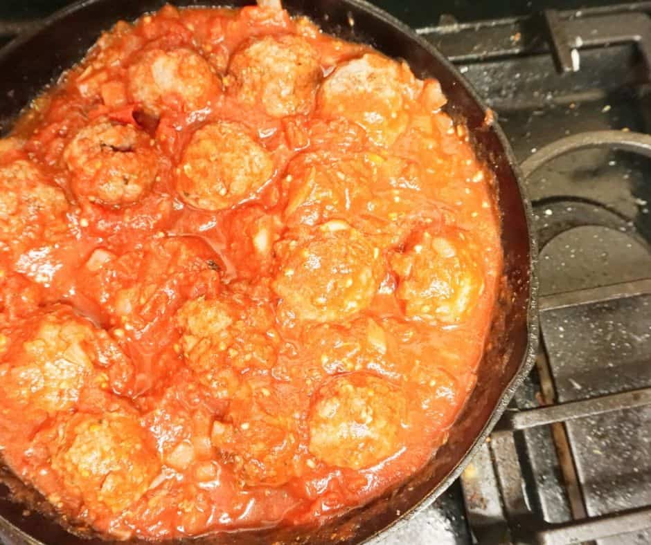 meatballs cooking in sauce in skillet on stovetop