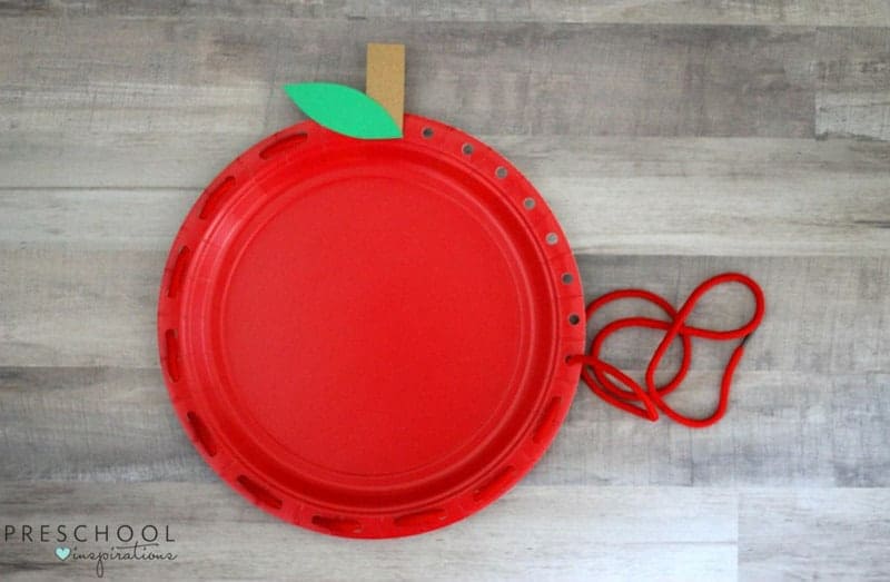 painted paper plate craft in the shape of an apple with lacing for fine motor skill development finished example