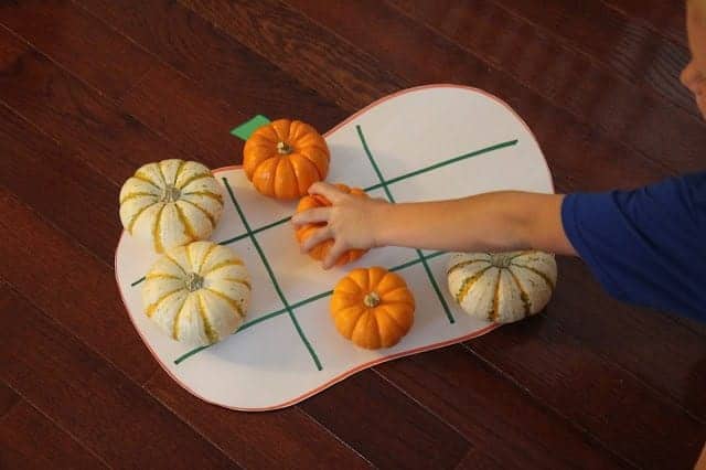 toddler hands playing tic tac toe on a giant cut out pumpkin with multi colored gourds instead of X's and O's