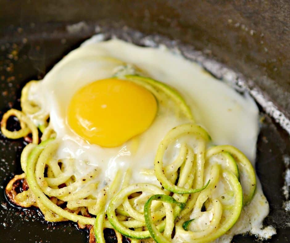 sunny side up egg cooking on top of a bed of zoodles in a cast iron skillet